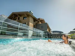 Frau entspannt im Außen-Whirlpool eines alpinen Wellnesshotels mit Bergblick