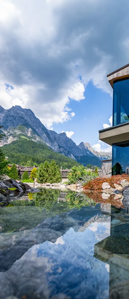 Modernes Berghotel mit Glasfassade mit Blick auf Teich und Alpenlandschaft
