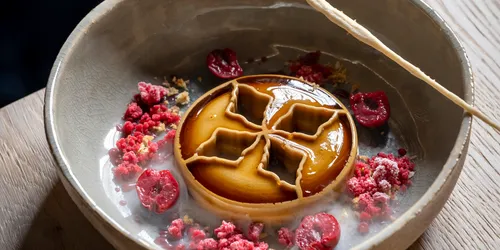 Gourmet-Dessert mit Karamellglasur, Himbeerkrümeln und dekorativem Gebäck in Keramikschale