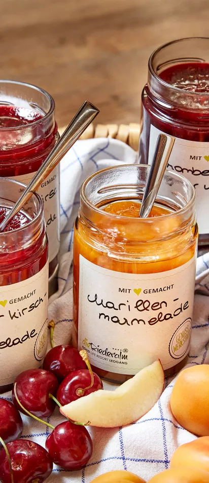 Basket with assorted jam jars and fresh fruit on a kitchen towel