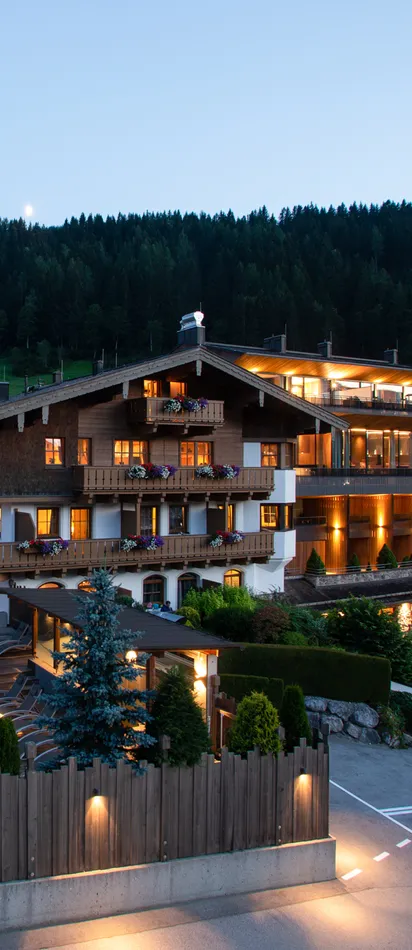 Beleuchtetes Alpenhotel mit Außenpool und Balkonen bei Sonnenuntergang