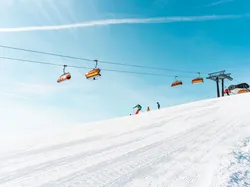 Skiers on a snowy slope under orange ski lifts and clear blue sky