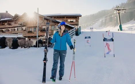 Frau in Skikleidung mit Skiern vor Chalet im sonnigen Skigebiet