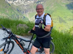 Älterer Radfahrer mit Mountainbike auf Alpenstraße vor schneebedeckten Gipfeln