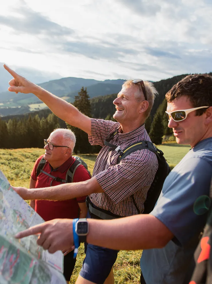 Group of hikers reading a map and pointing toward mountains in scenic alpine landscape