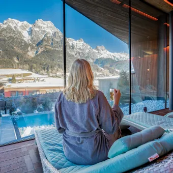 Frau entspannt im Spa mit Blick auf verschneite Berge und Außenpool im Winter