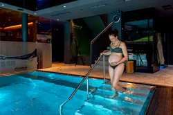 Pregnant woman in bikini smiling while entering indoor spa pool