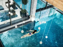 Frau schwimmt in einem luxuriösen Spa-Innenpool mit modernem Glasdesign