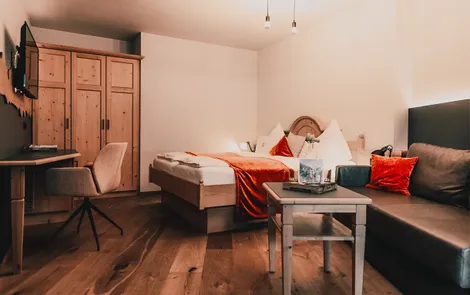Gemütliches Hotelzimmer mit Holzboden, Doppelbett, Sofa und Schreibtisch mit Stuhl
