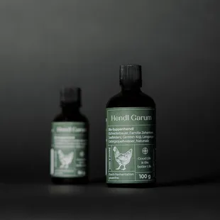 Zwei Flaschen Hendl Garum Hühnerwürzsauce vor dunklem Hintergrund