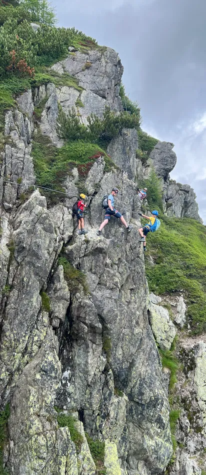 Group of climbers scaling rocky mountain wall with safety harnesses under cloudy sky