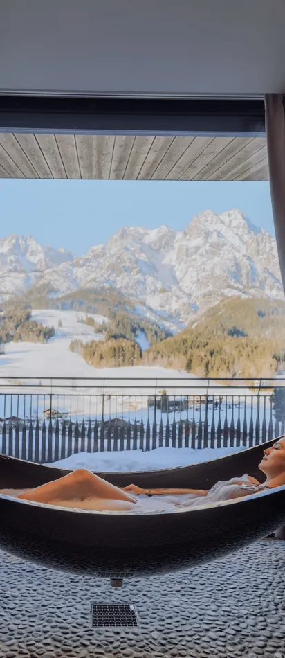 Frau entspannt in einer Hängematten-Badewanne mit Blick auf verschneite Berge im Luxus-Spa