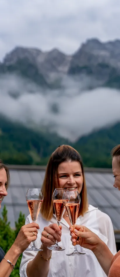 Frauen stoßen mit Rosé-Champagner auf einer Terrasse mit Bergblick an
