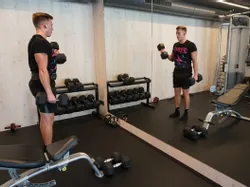 Mann macht Kurzhantel-Curls im modernen Fitnessstudio vor einem Spiegel