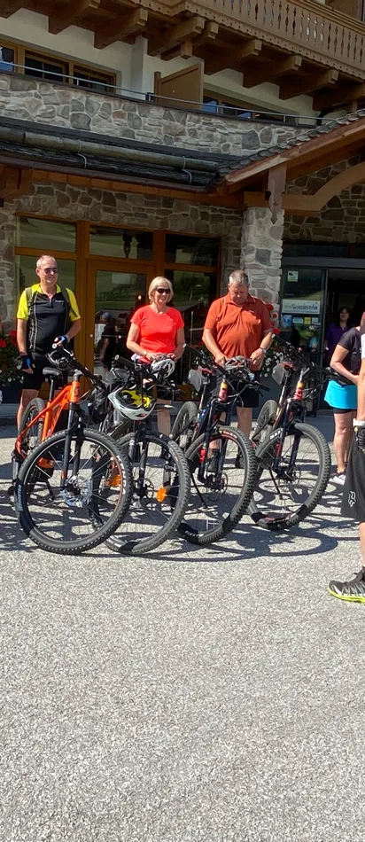Gruppe von Radfahrern mit Mountainbikes vor einer rustikalen Lodge bei sonnigem Wetter