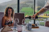 Waiter pouring red wine at a restaurant table with mountain view