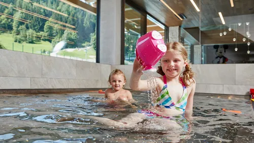 Two children playing with water toy in indoor pool at family hotel in the Alps