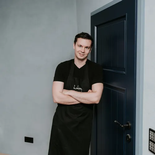 Young man in black apron leaning against a blue door