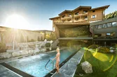 Frau am Außenpool eines Luxushotels mit Bergblick und Sonnenlicht im Hintergrund