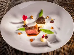 Gourmet beef dish with mashed potatoes, sugar snap peas, and edible flowers on white plate