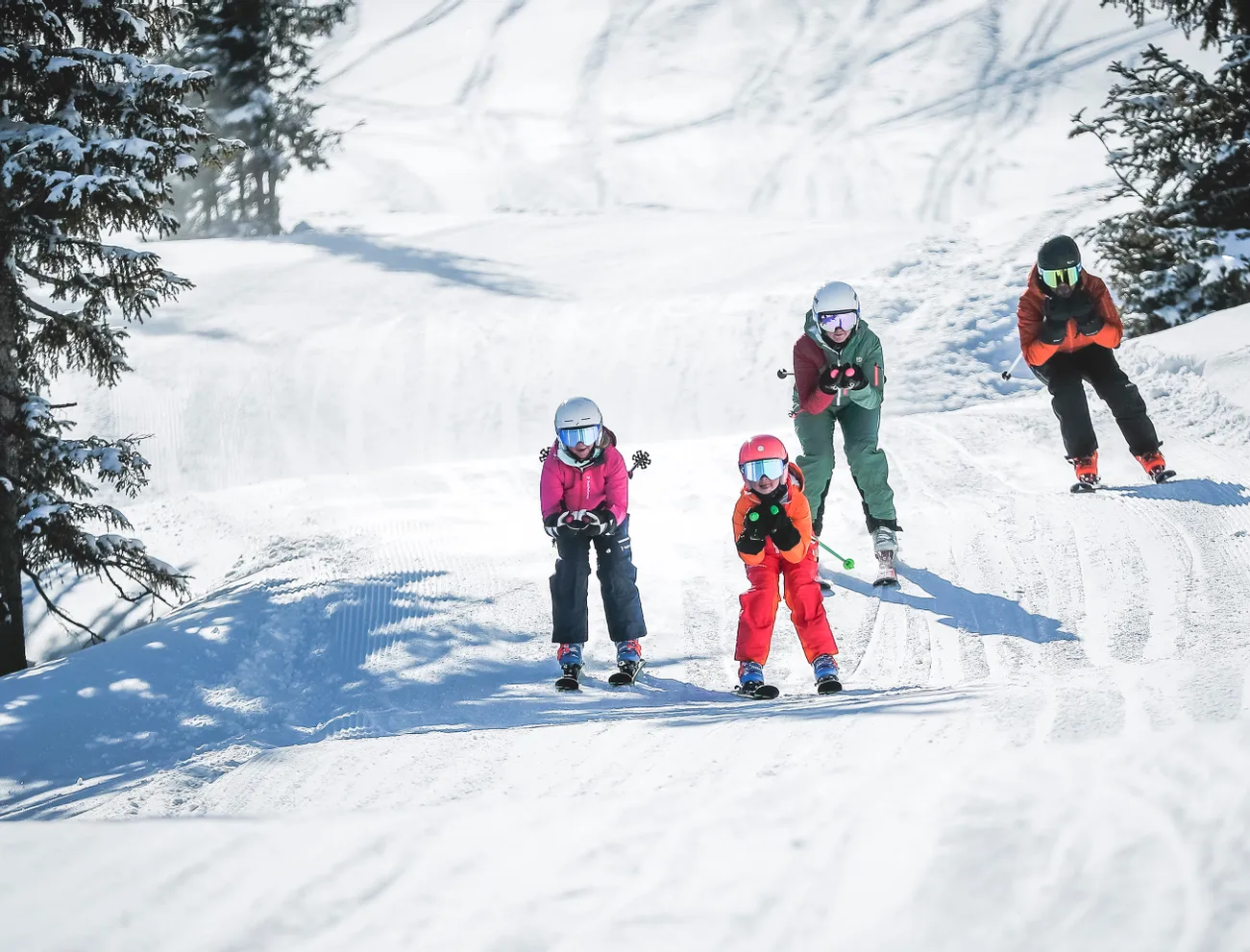 Familie fährt gemeinsam Ski auf einem verschneiten Berghang bei Sonnenschein