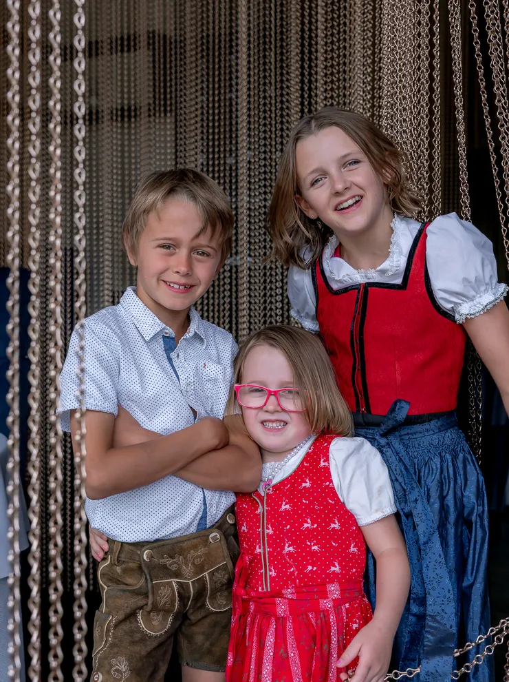 Smiling children in traditional Bavarian clothing standing in front of beaded curtain