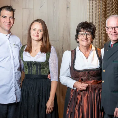 Group portrait of four adults in traditional Austrian attire, standing indoors and smiling at camera