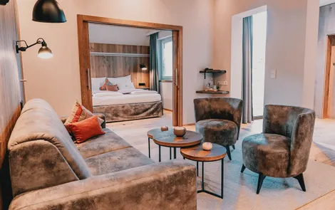 Modern hotel suite with cozy lounge, velvet furniture and view into bedroom