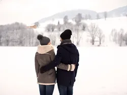 Couple in winter clothing embracing while standing in snowy mountain landscape