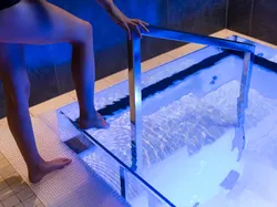 Person stepping into cold plunge pool with stainless steel handrail under blue lighting