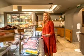 Lächelnde Frau im roten Kleid wählt Speisen am Hotel-Frühstücksbuffet mit Wurst und Gebäck