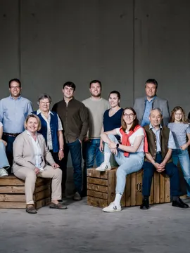 Mehrgenerationenfamilie steht und sitzt vor grauer Wand auf Holzkisten