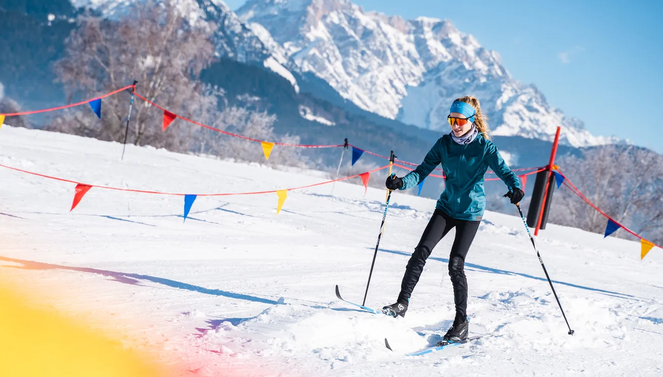 Woman cross-country skiing on a snowy trail with alpine mountains in the background