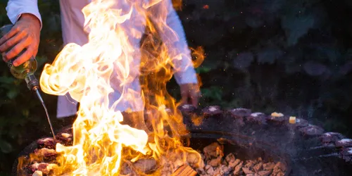 Koch grillt Blaubeer-Nocken über offenem Feuer mit Flammen an einem Outdoor-Grill
