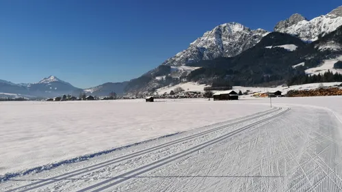 Cross-country ski trail through snowy landscape with Alps and clear blue sky
