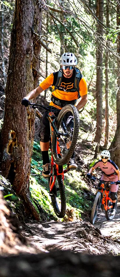 Mountain bikers riding a forest trail with one lifting the front wheel on a dirt path