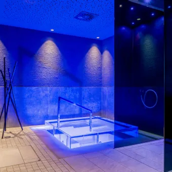 Modern indoor spa room with blue ambient lighting and a sunken hot tub