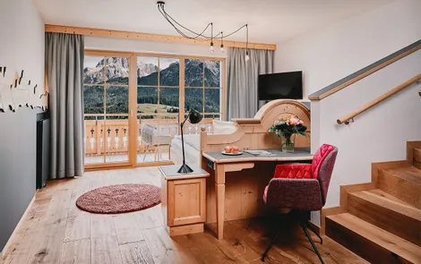 Gemütliches Hotelzimmer mit Schreibtisch, Holzboden und Blick auf die Alpen