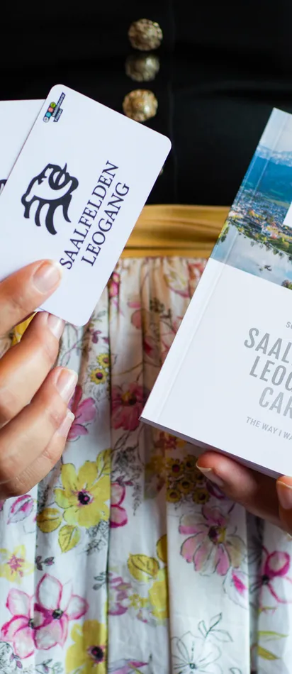 Frau in Tracht hält Saalfelden Leogang Card und Broschüre für 2024–2025