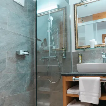 Modern hotel bathroom with glass shower, sink, mirror and folded white towels