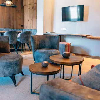Modern hotel lounge with grey velvet chairs, wooden tables and wall-mounted TV