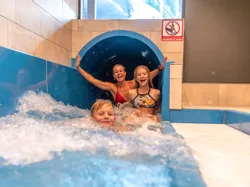 Family laughing as they exit an indoor water slide into a pool