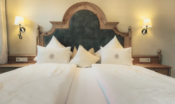 Cozy hotel bed with embroidered pillows, wooden headboard and warm wall lighting