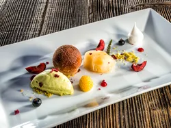 Gourmet-Dessert mit Kugeln aus Eis und Sorbet, Früchten und Baiser auf weißem Teller