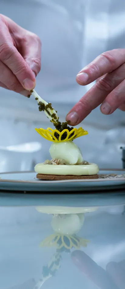 Pâtissier richtet Gourmet-Dessert mit gelber Zuckerdekoration und Garnitur an