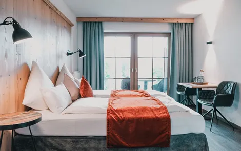 Modern hotel room with double bed, red throw blanket, desk and balcony access