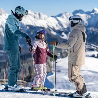 Three skiers talking on a sunny ski slope in the snowy Alps mountains