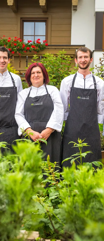 Team von Köchen in gestreiften Schürzen steht im Kräutergarten vor einem Alpenrestaurant