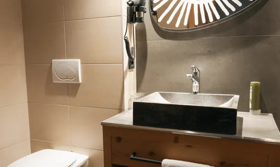 Modern bathroom with wall-mounted toilet, vessel sink, and decorative mirror with backlight