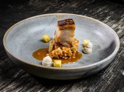 Gourmet dish with braised pork belly, vegetable pearls and artistic puree on ceramic plate